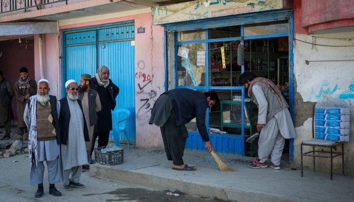 Pessoas removem cacos de vidro de sua loja, após um ataque aéreo paquistanês, no bairro de Dar...