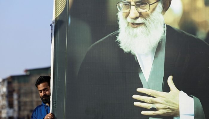 Um homem segura a foto do líder supremo do Irã, aiatolá Ali Khamenei, enquanto muçulmanos xii...